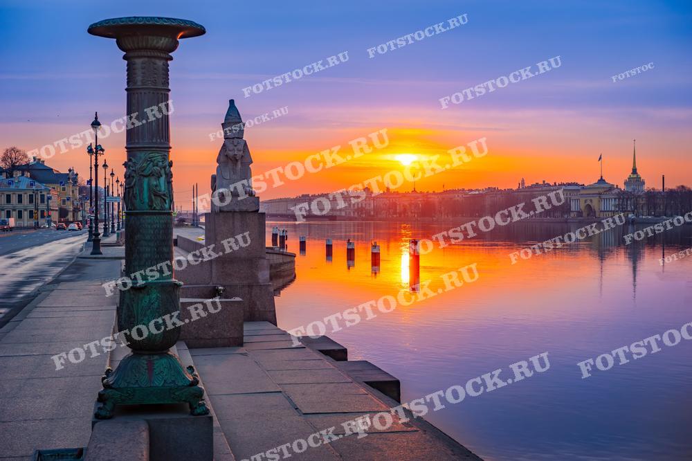 На фотографии запечатлен рассвет на набережной в Санкт-Петербурге. Нежные оттенки рассветного неба и золотистые лучи солнца отражаются в спокойных водах реки, создавая волшебное настроение. Фотография подойдет для использования в туристических брошюрах, для украшения интерьера или в качестве иллюстративного материала в статьях о городе.